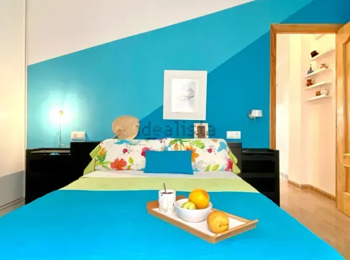 Dormitorio con pared pintada de azul y blanco, cama con bandeja de fruta. Puerta al pasillo.