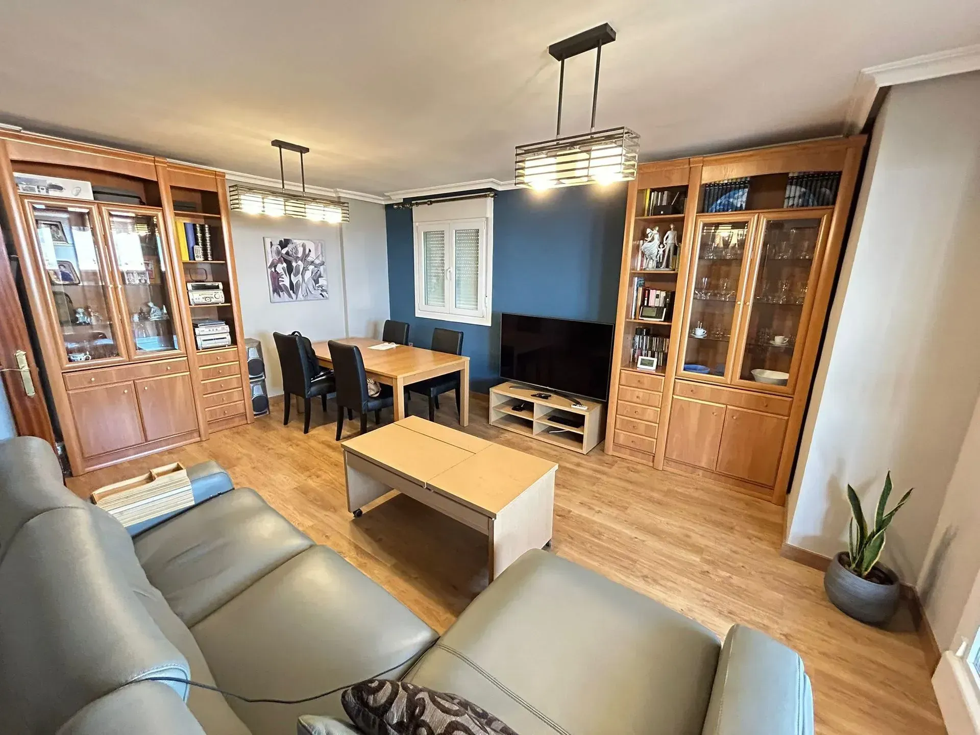 Sala de estar con muebles de madera, mesa de comedor, sofá gris y TV.