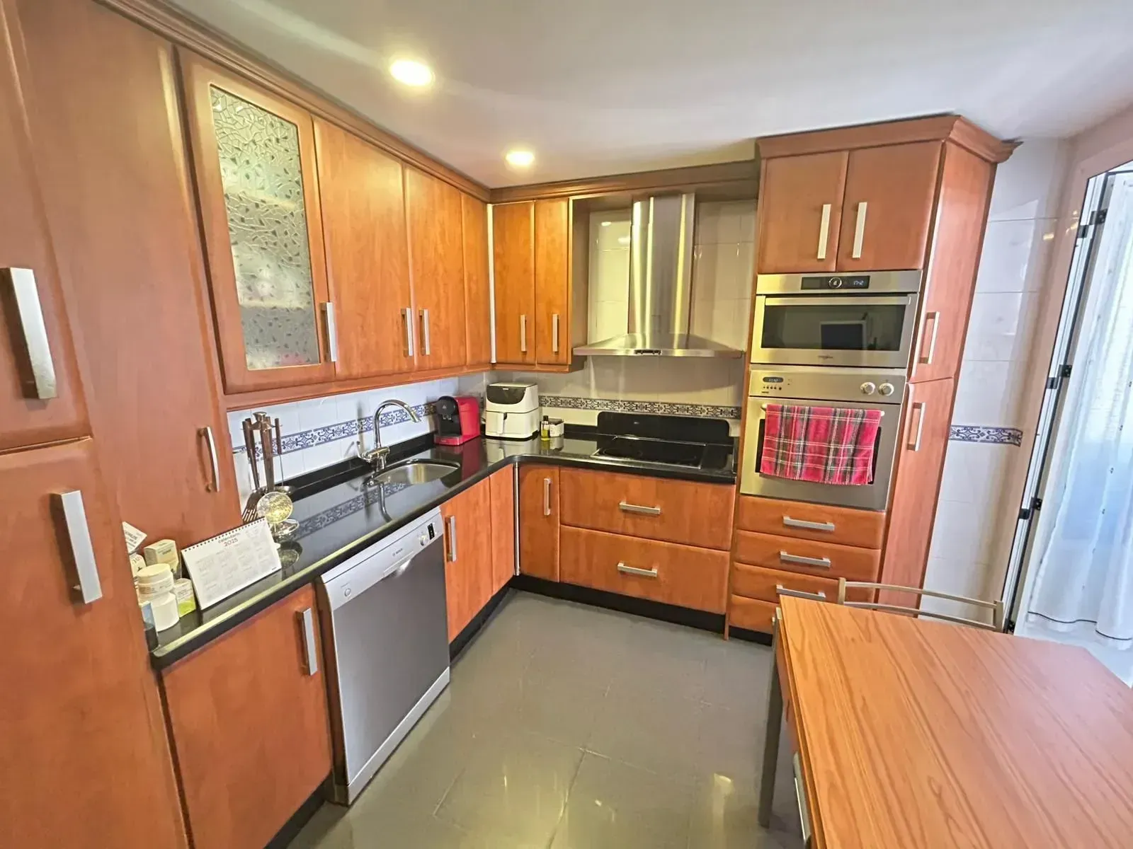 Cocina con gabinetes de madera, electrodomésticos de acero inoxidable y encimeras negras.