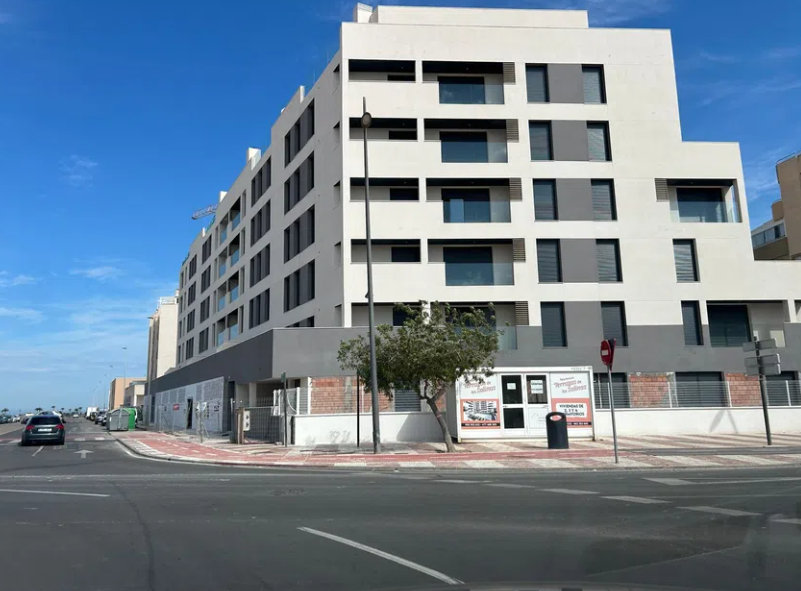 Habitación vacía con suelo de madera, ventanal con balcón y puerta de entrada.