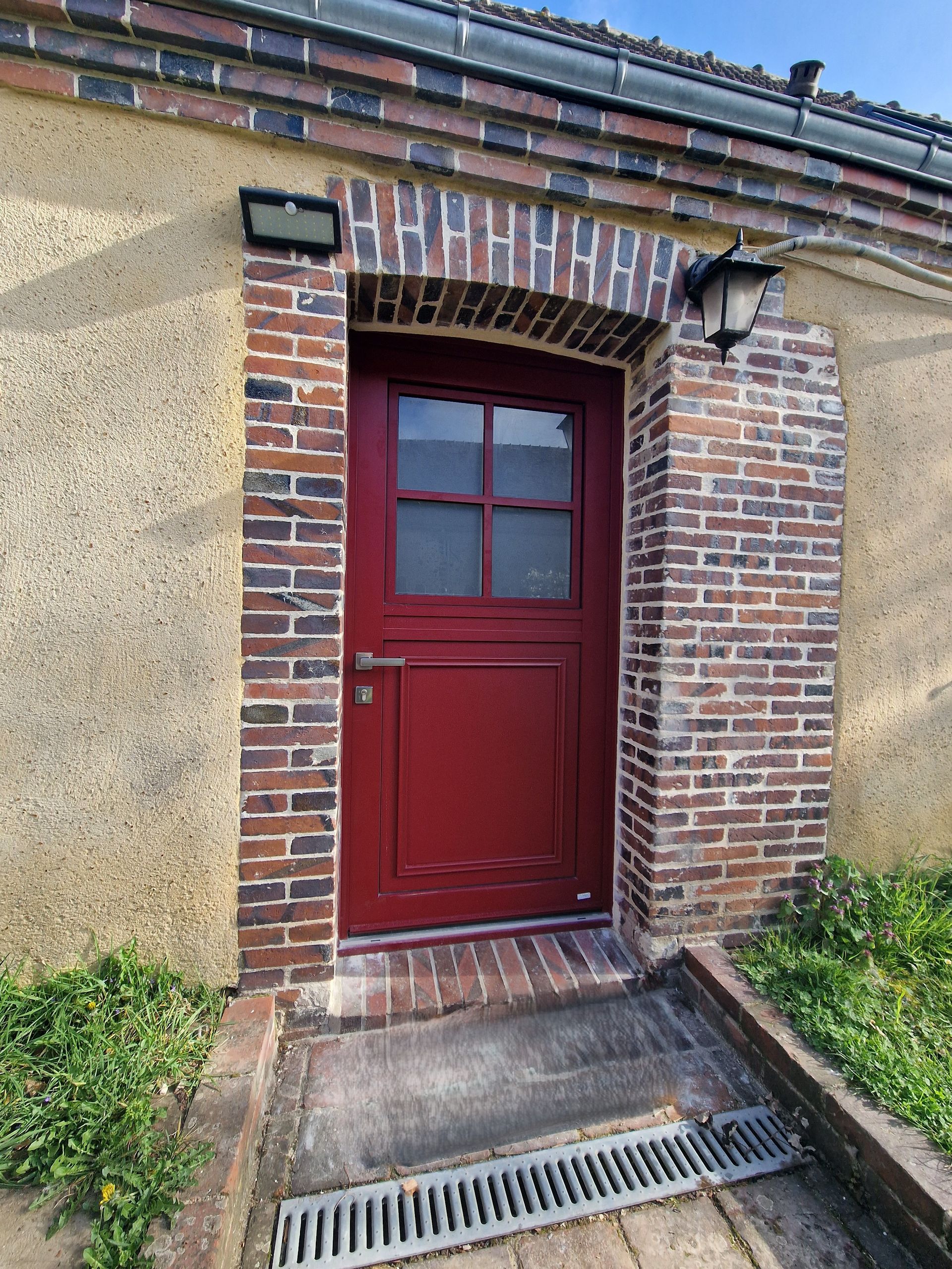 Porte d'entrée rouge avec petite fenêtre intégrée à l'entrée d'un bâtiment en briques et en stuc
