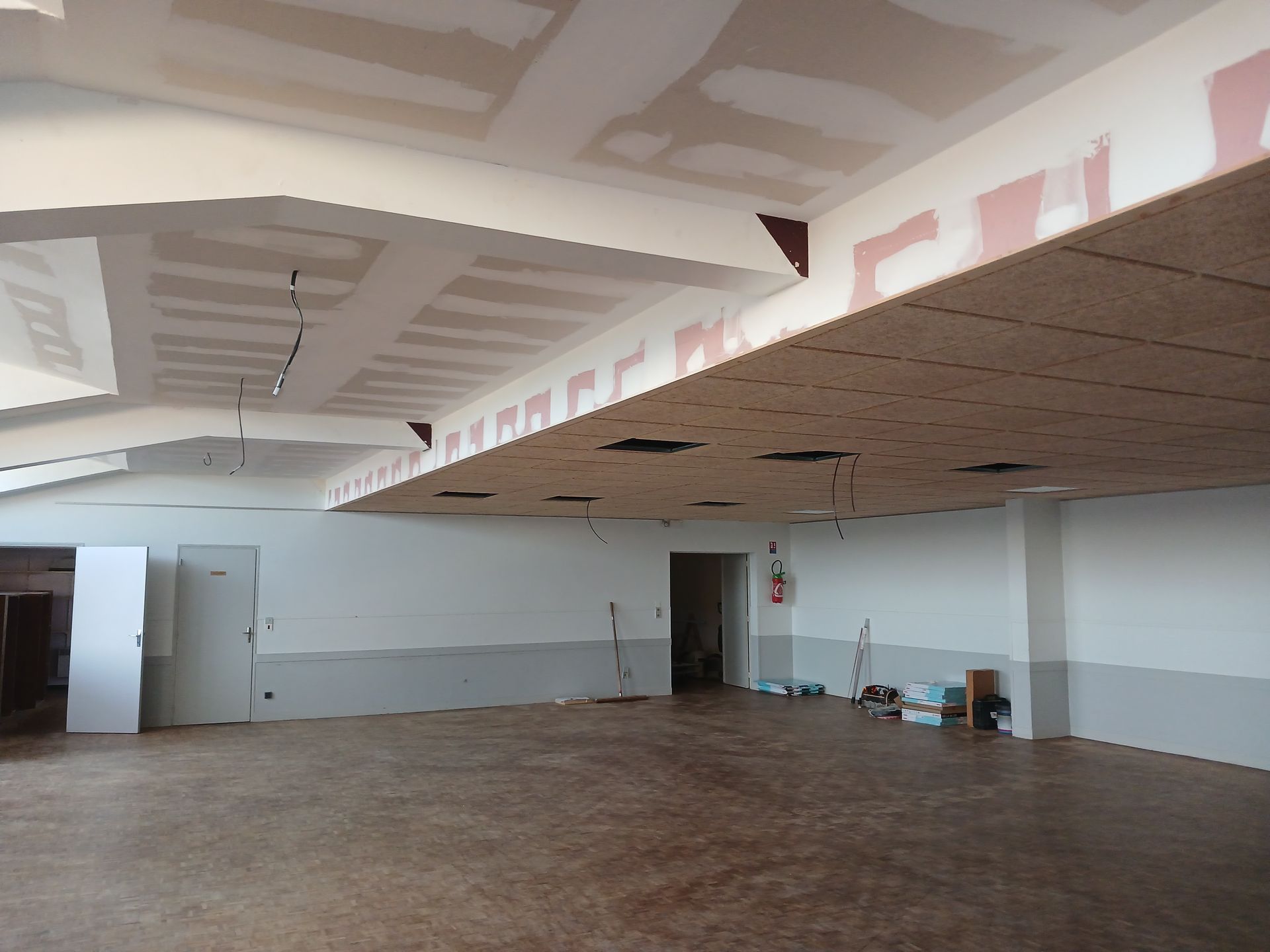 Pièce vide et inachevée avec plafond apparent, murs blancs et matériaux de construction au sol
