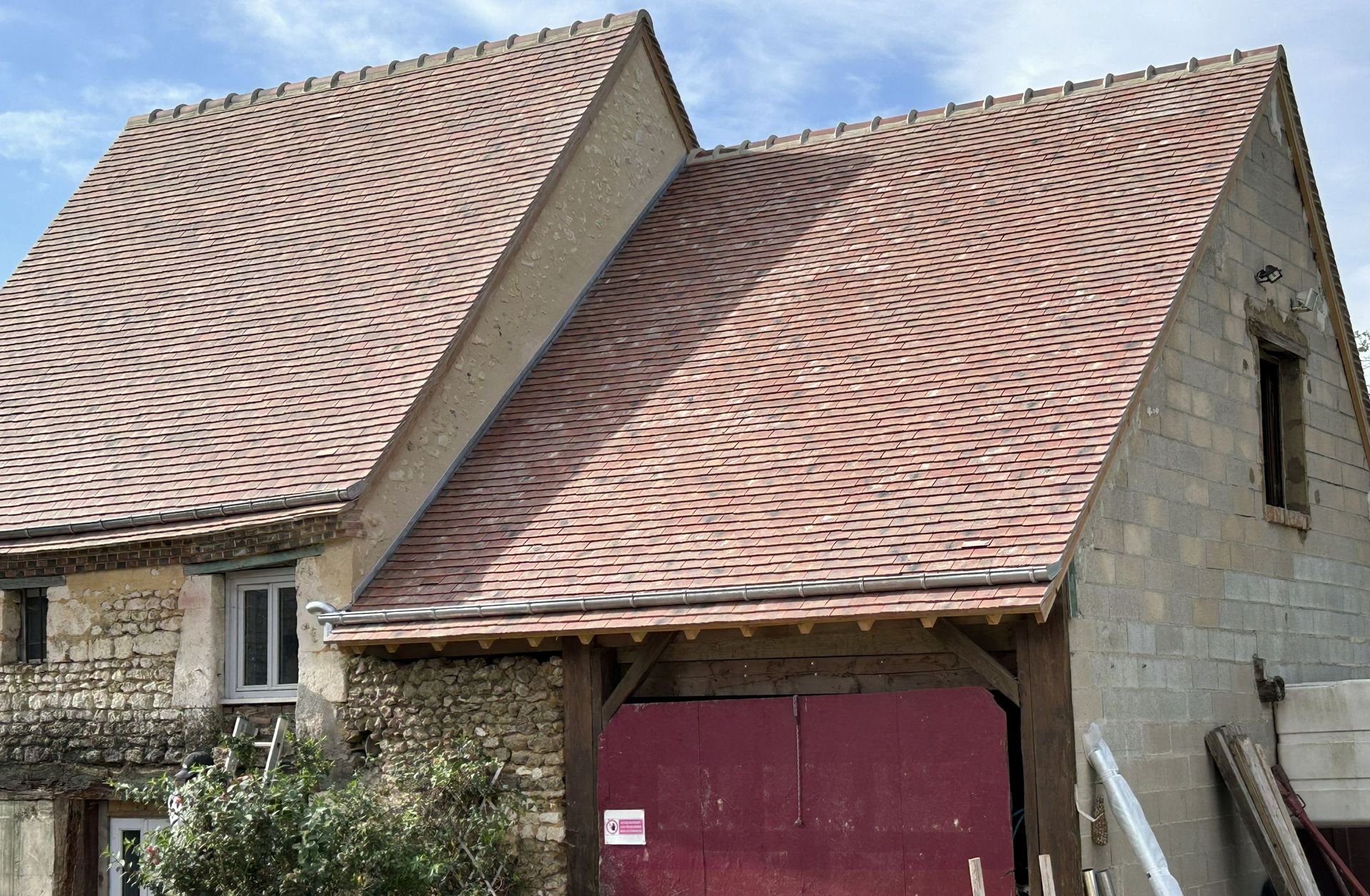 Deux maisons en pierre mitoyennes aux toits pentus de tuiles rouges et à la porte de garage bordeaux.