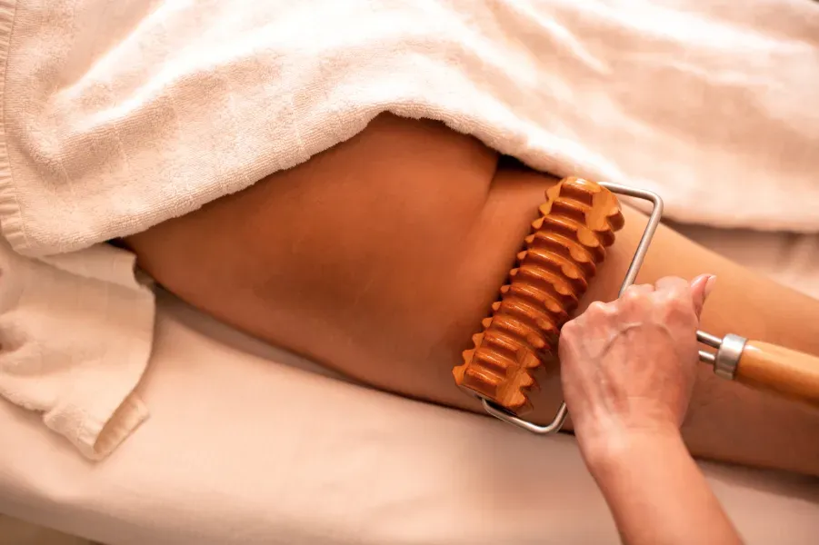 Durante un tratamiento de spa, una persona utiliza un rodillo de masaje de madera en el muslo de un cliente.