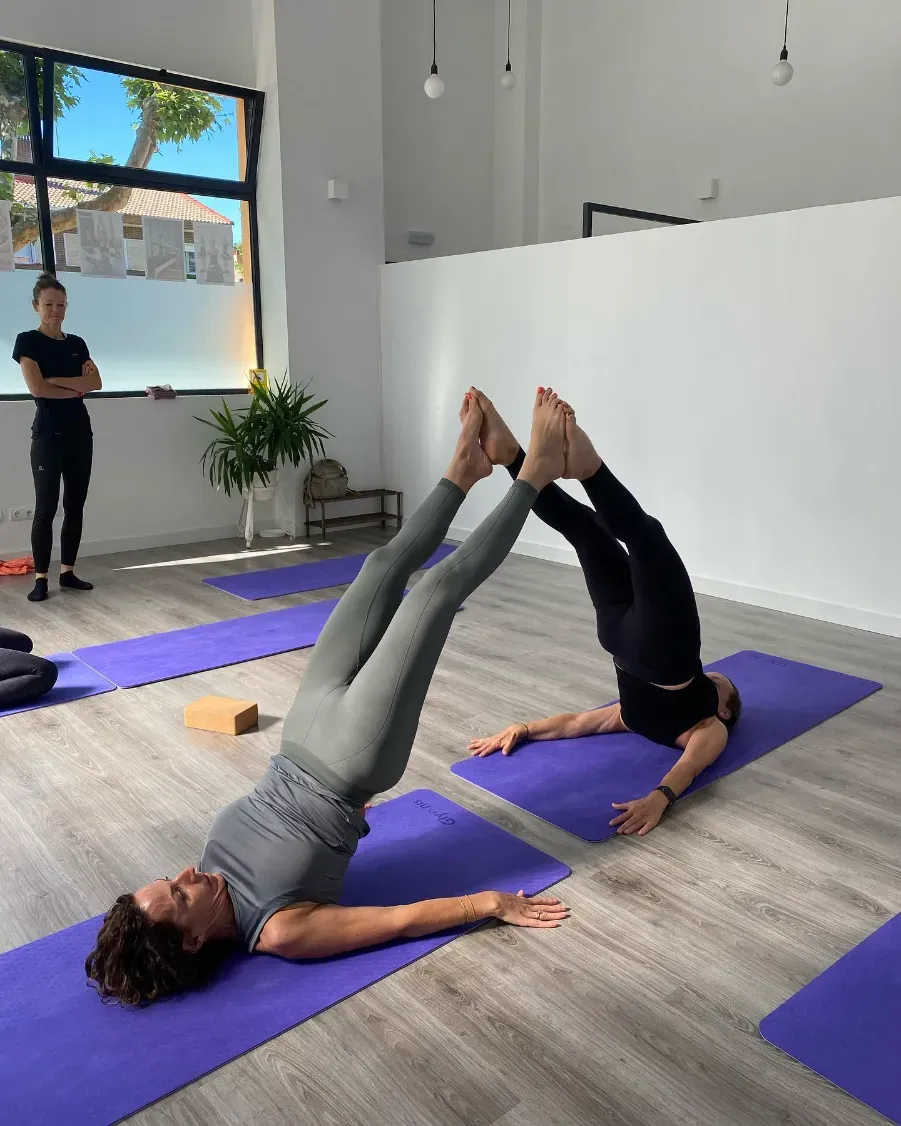 Dos personas haciendo Pilates en máquinas en un estudio, sujetando barras y tirando de resortes.