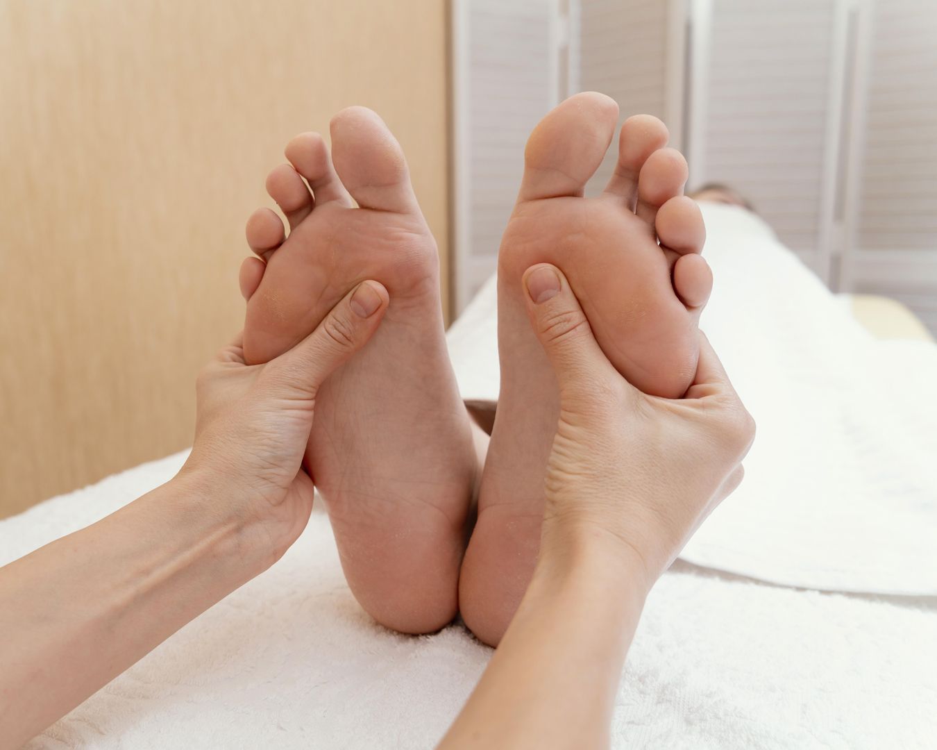 Las manos de un terapeuta masajean las plantas de los pies de una persona sobre una camilla de masaje.
