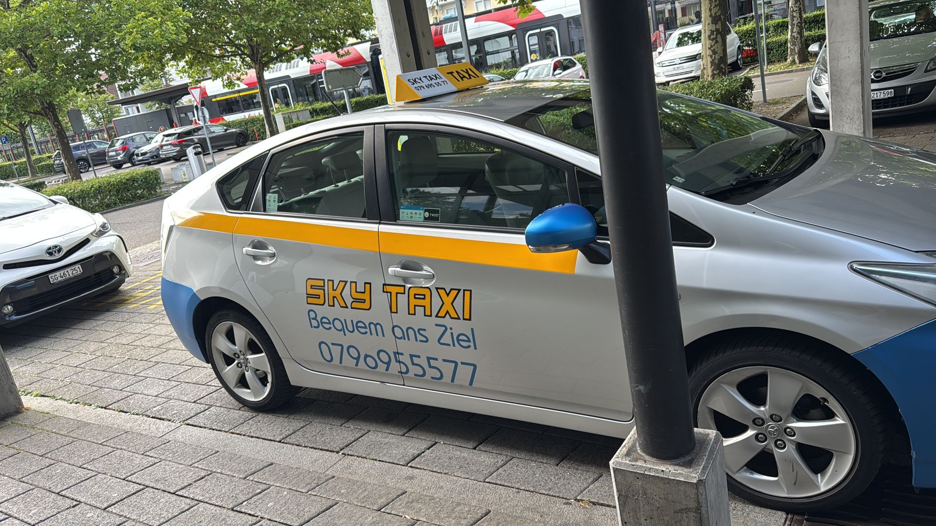 Auf einem gepflasterten Gehweg parkt ein weiß-blaues Taxi.