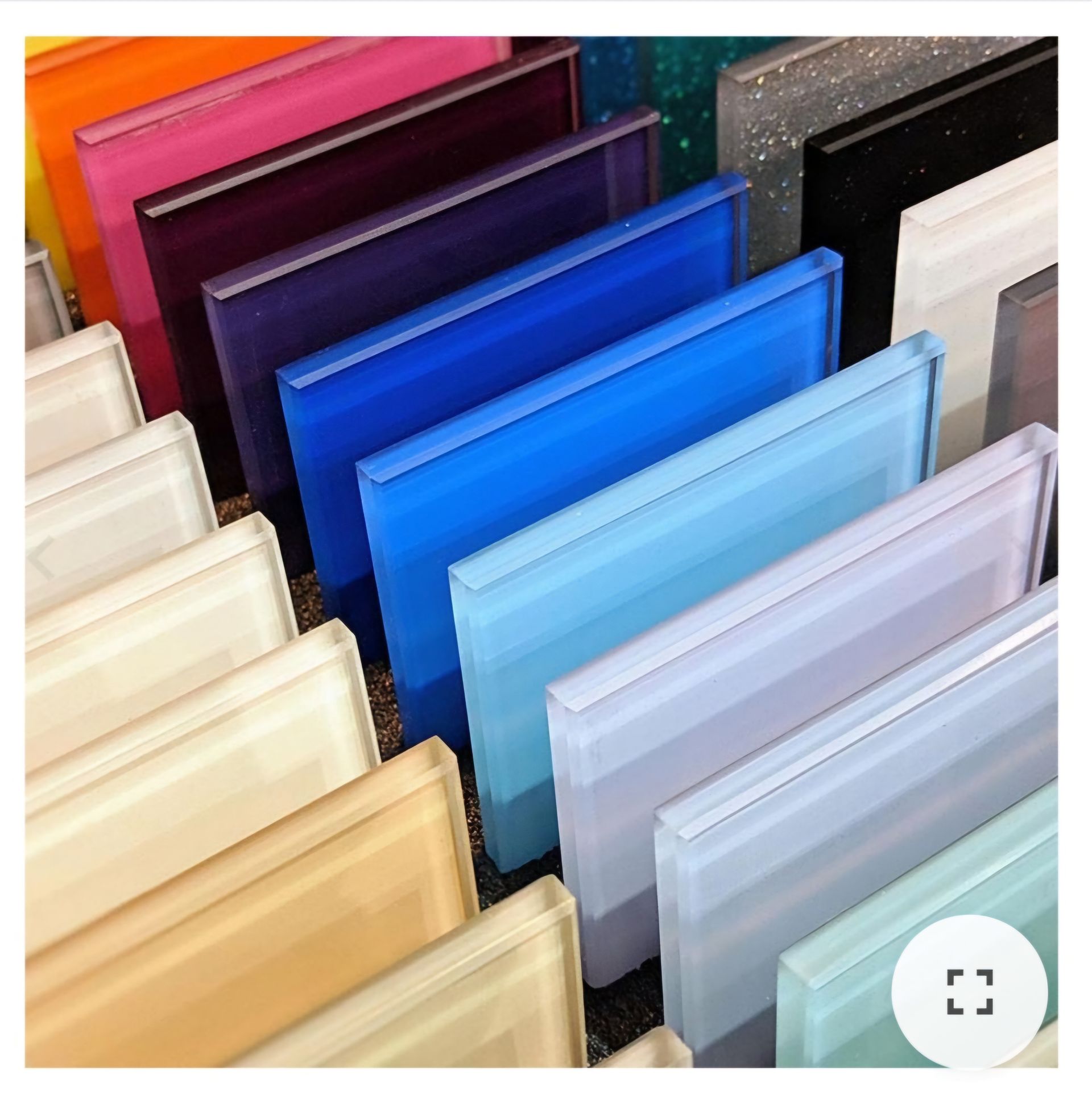 Des carreaux de verre translucides de couleurs variées, alignés en rangée, présentant une gamme de bleus, de violets et de tons neutres.