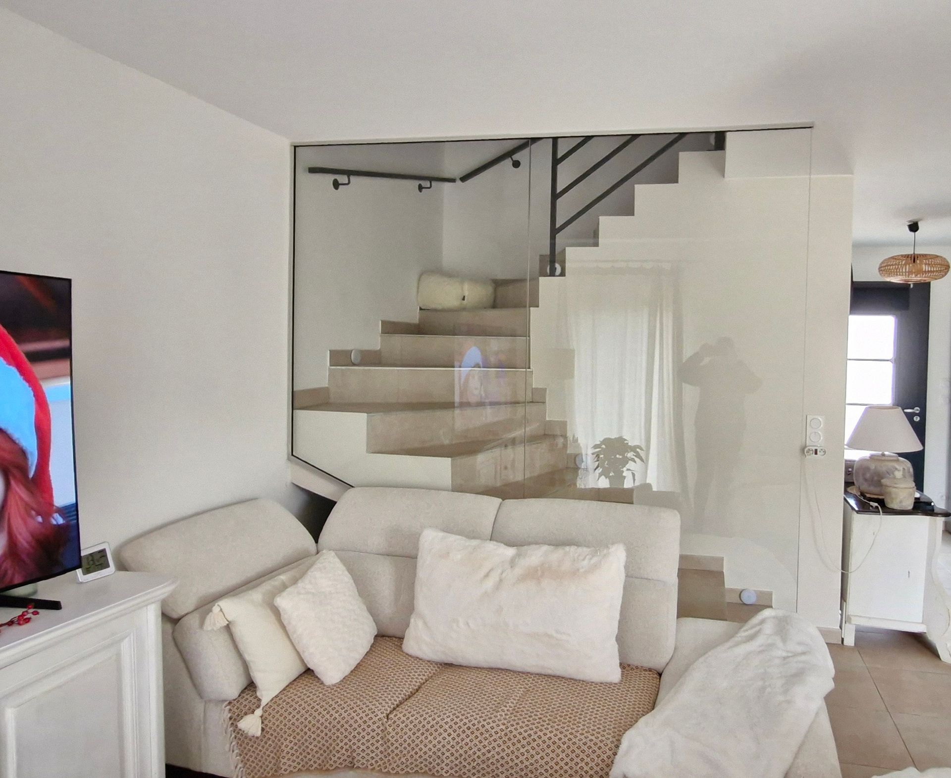 Salon confortable avec canapé couleur crème, escalier au garde-corps de verre