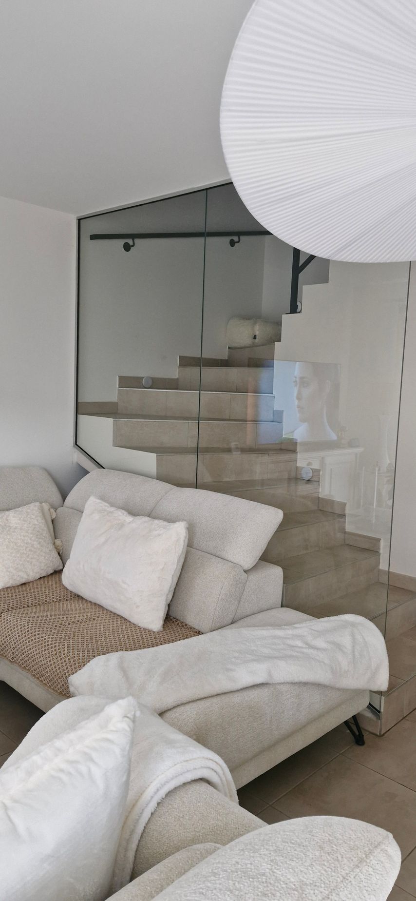 Un salon moderne avec un canapé gris clair et un escalier vitré