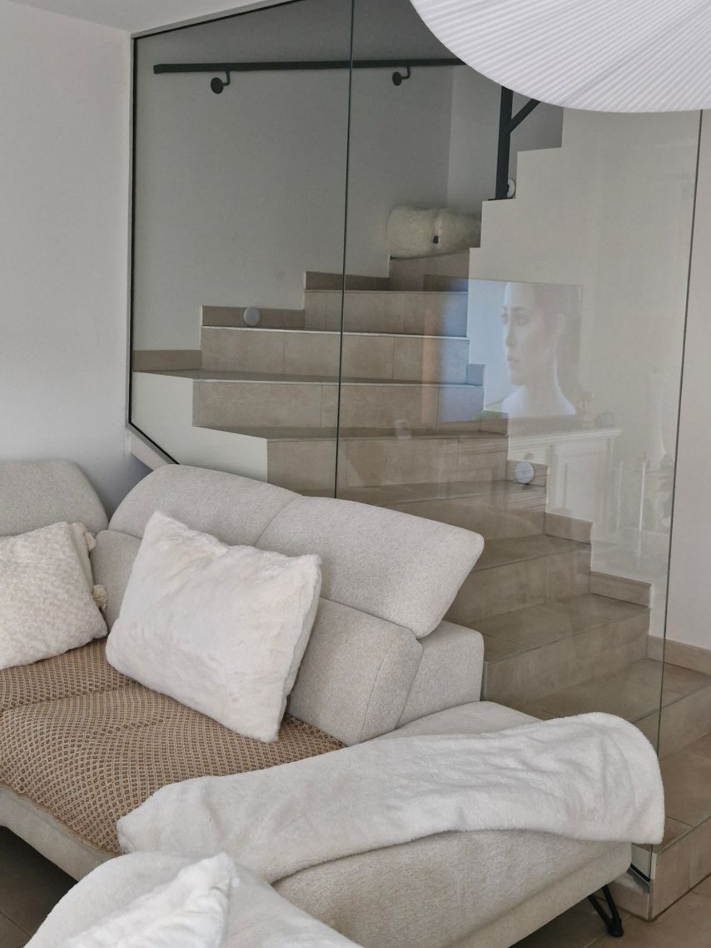 Cloison intérieure en verre transparent séparant un escalier et un salon avec aménagement contemporain.