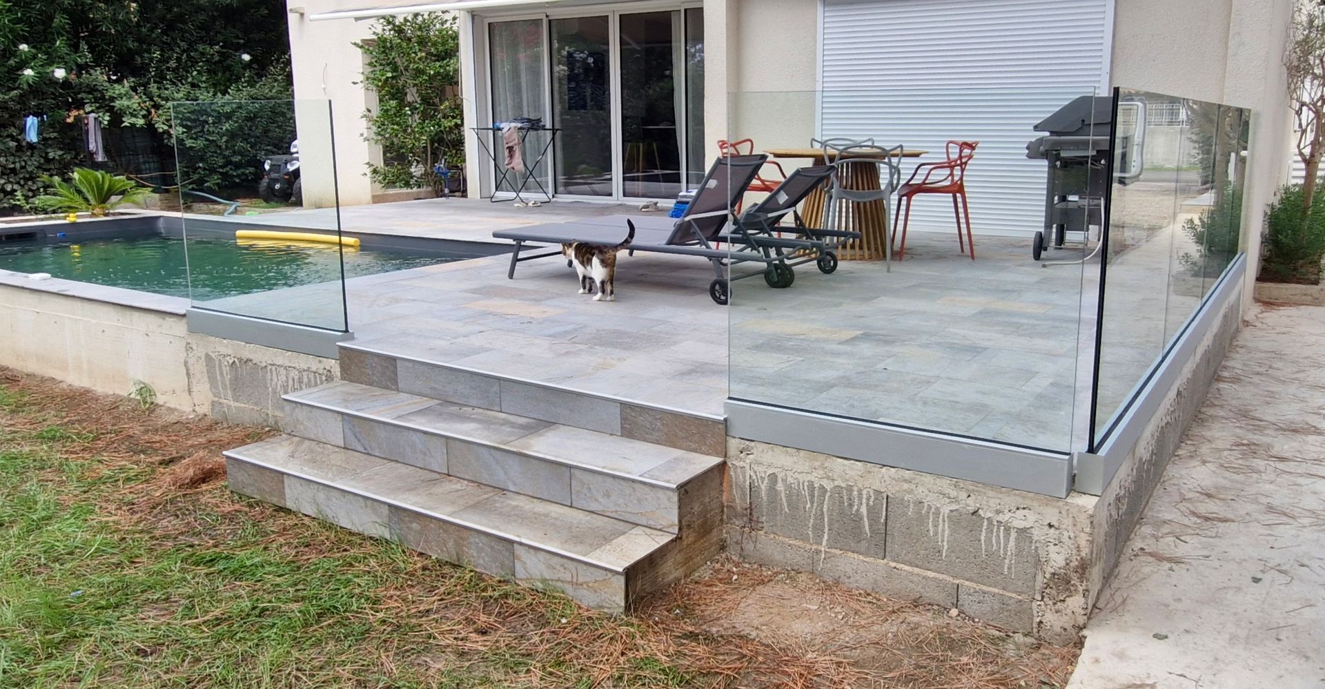 Terrasse avec balustrade en verre, marches, piscine et chaises longues