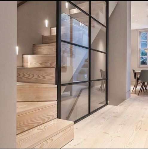 Verrière intérieure en acier avec vitrage clair séparant un escalier en bois et un espace de vie.