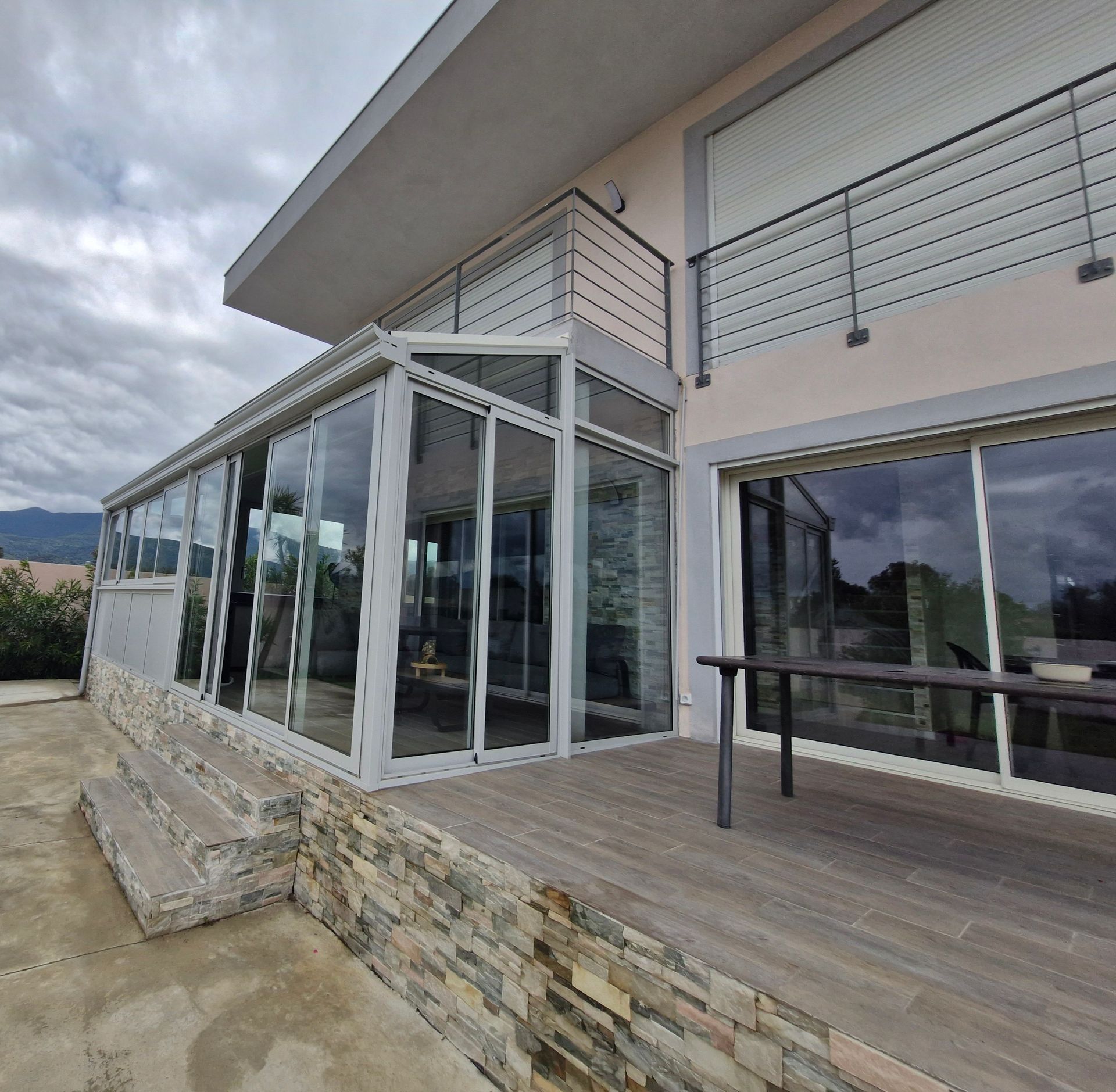 Vue extérieure d'une maison moderne avec une véranda vitrée et un balcon avec garde-corps métallique
