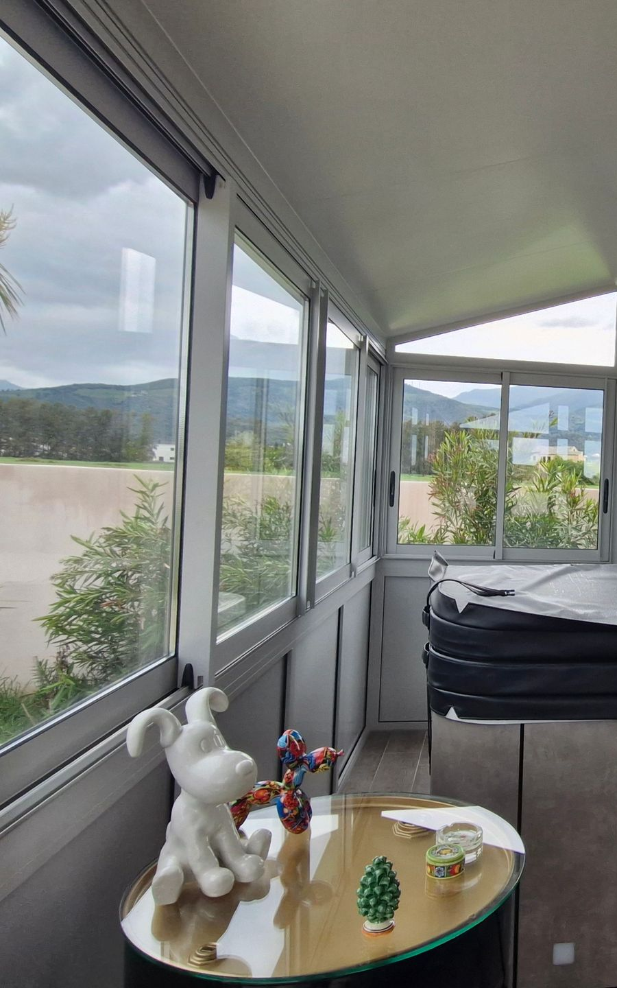 Espace fermé type véranda équipé de grandes surfaces vitrées en aluminium avec vue sur un jardin.