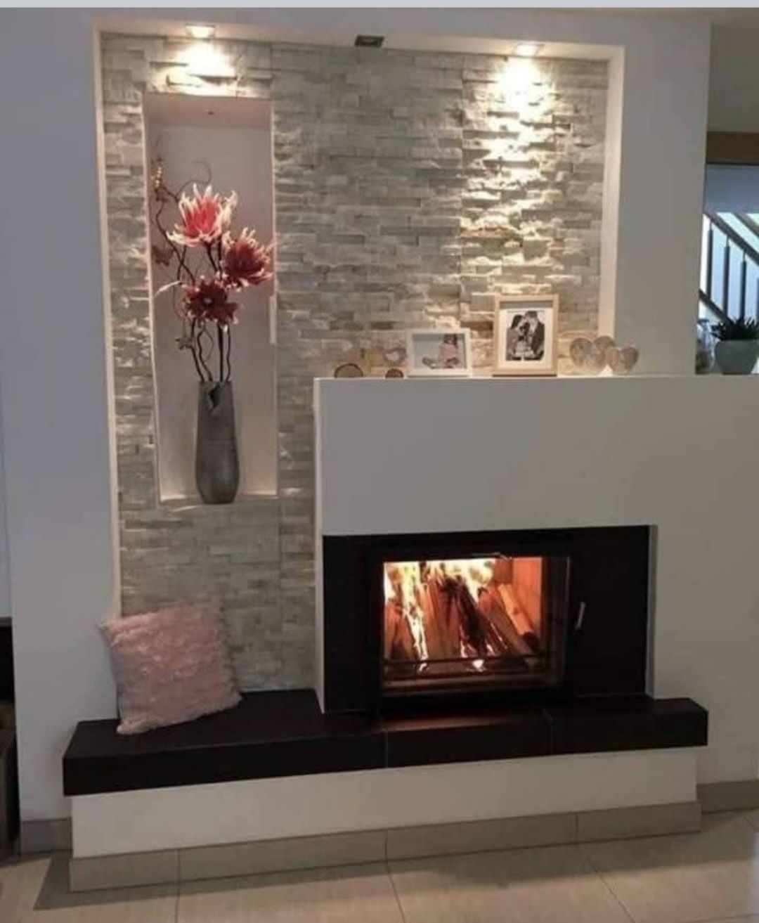 Cheminée avec mur en pierre, niche fleurie, feu allumé et décor blanc, noir et gris clair