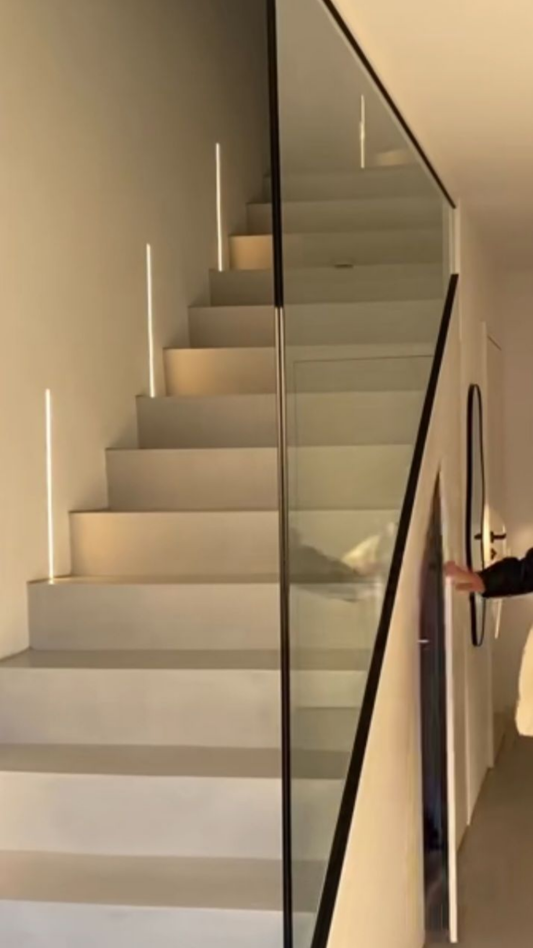 Escalier avec rampe en verre, design moderne. Marches éclairées, murs aux couleurs neutres, porte à droite.