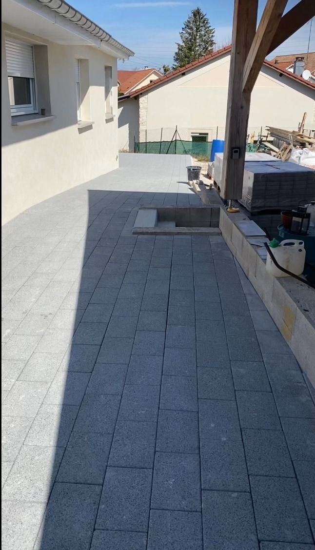 Patio en pierre grise en cours de construction à côté d'une maison de couleur claire.