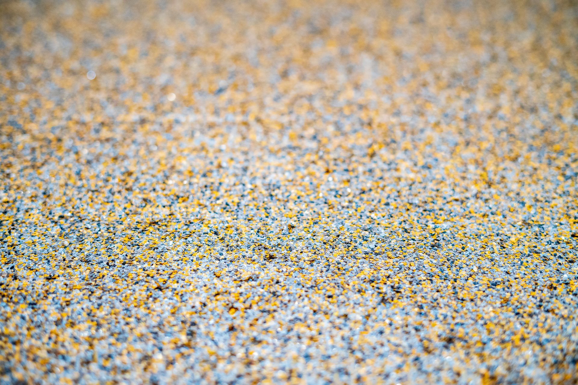 Gros plan sur une surface texturée avec de petits granules multicolores, principalement bleus, jaunes et gris.