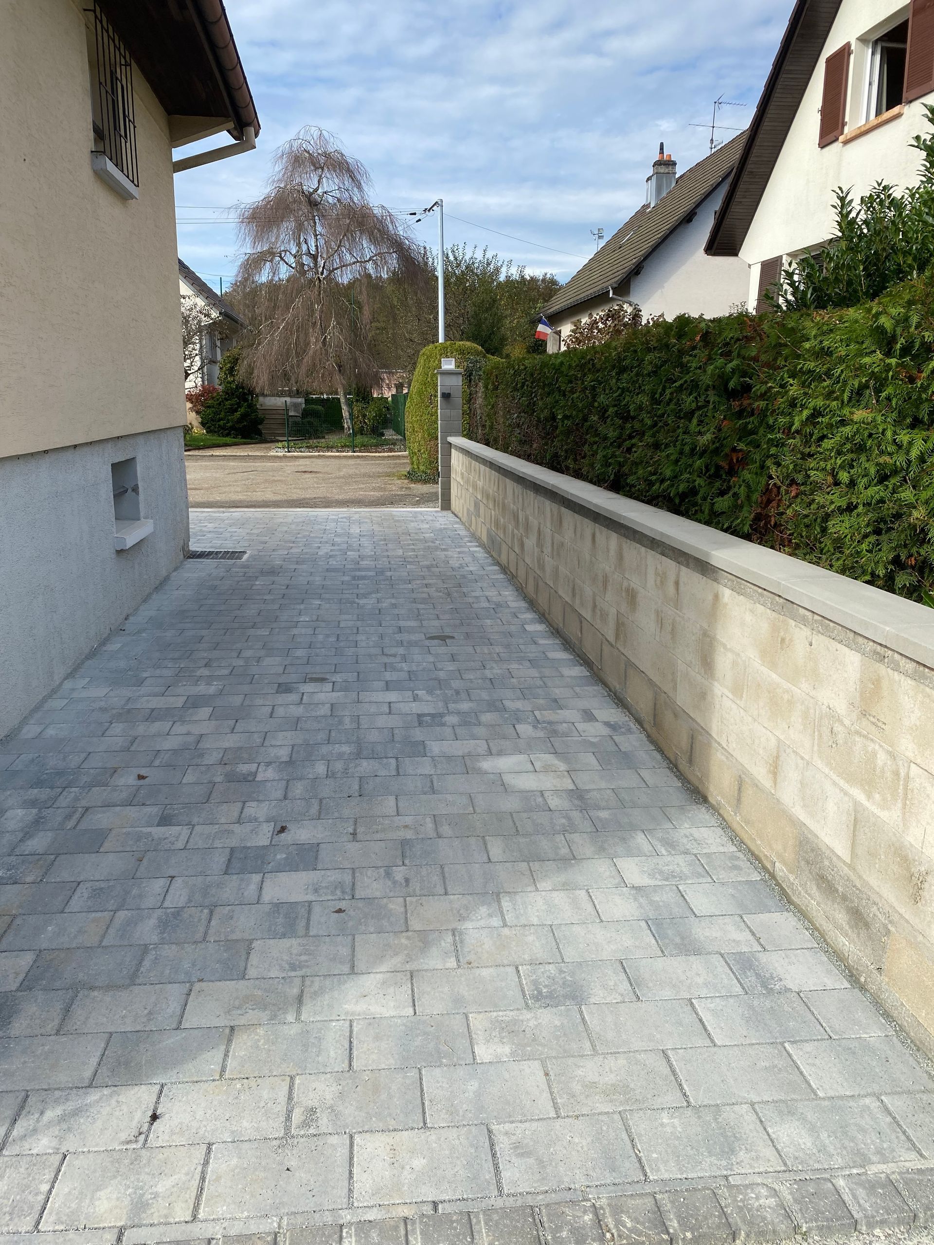 Chemin en briques grises à côté d'une maison en blocs de béton avec une clôture métallique sur la gauche.