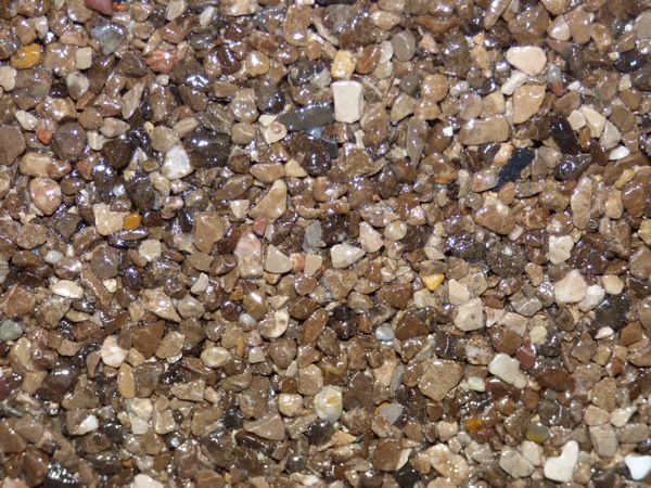 Gros plan sur du gravier brun et beige, de petits rochers avec des surfaces humides et réfléchissantes.