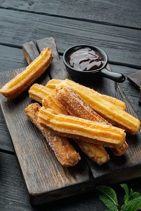 Churros con salsa de chocolate sobre una tabla de cortar de madera.