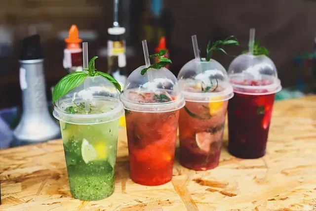 Una fila de vasos de plástico llenos de diferentes tipos de bebidas sobre una mesa de madera.