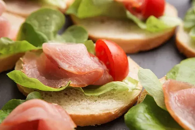 Un primer plano de un sándwich con jamón, lechuga y tomates.