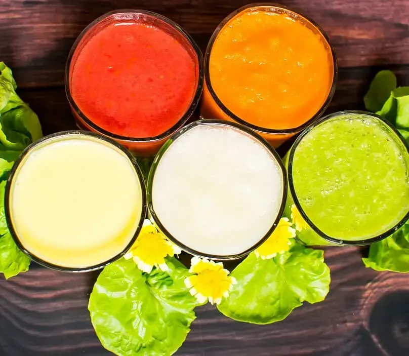 Cuatro vasos de jugos de diferentes colores están sobre una mesa de madera.
