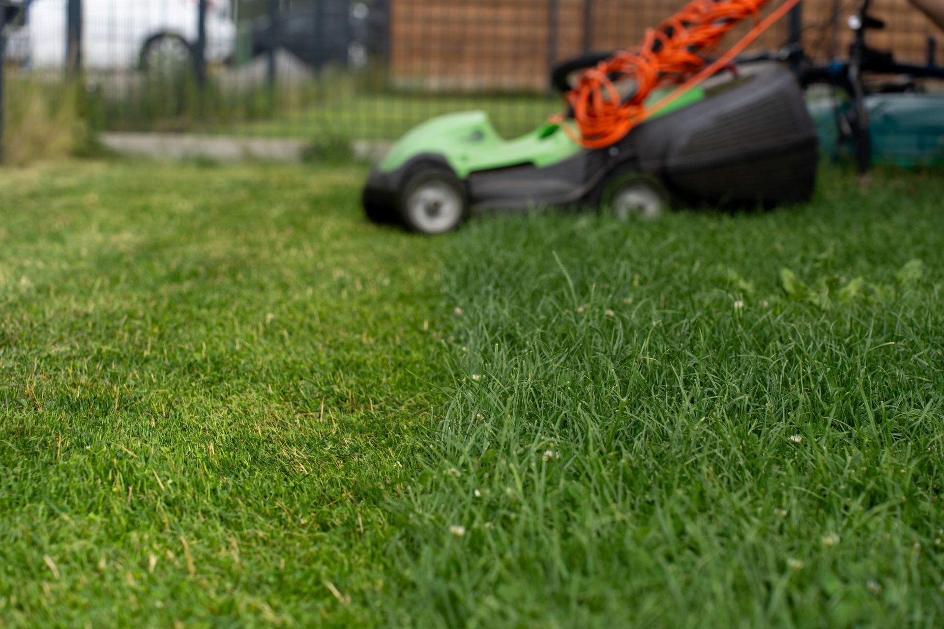 Pelouse verte tondue par une tondeuse vert et orange.