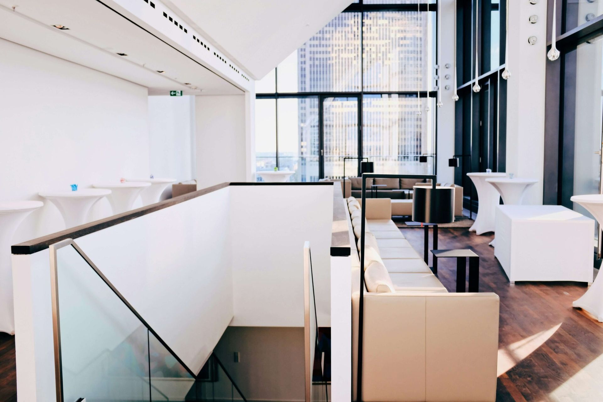 Intérieur moderne avec escalier, coin salon et vue sur la ville grâce à de grandes fenêtres. Les tons blancs et beiges dominent.