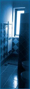 Baño de tonos azules con suelo de baldosas, toallero y una ventana luminosa junto a una puerta oscura.