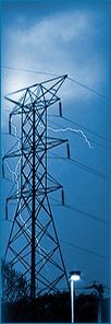 Torre de transmisión eléctrica contra un cielo azul con relámpagos al fondo.