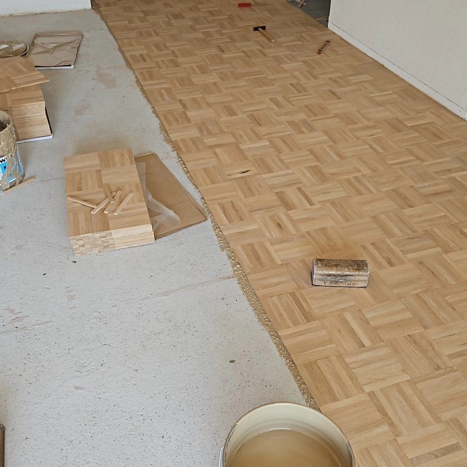 Pose d'un parquet en bois clair dans une pièce avec une dalle de béton et des outils éparpillés.