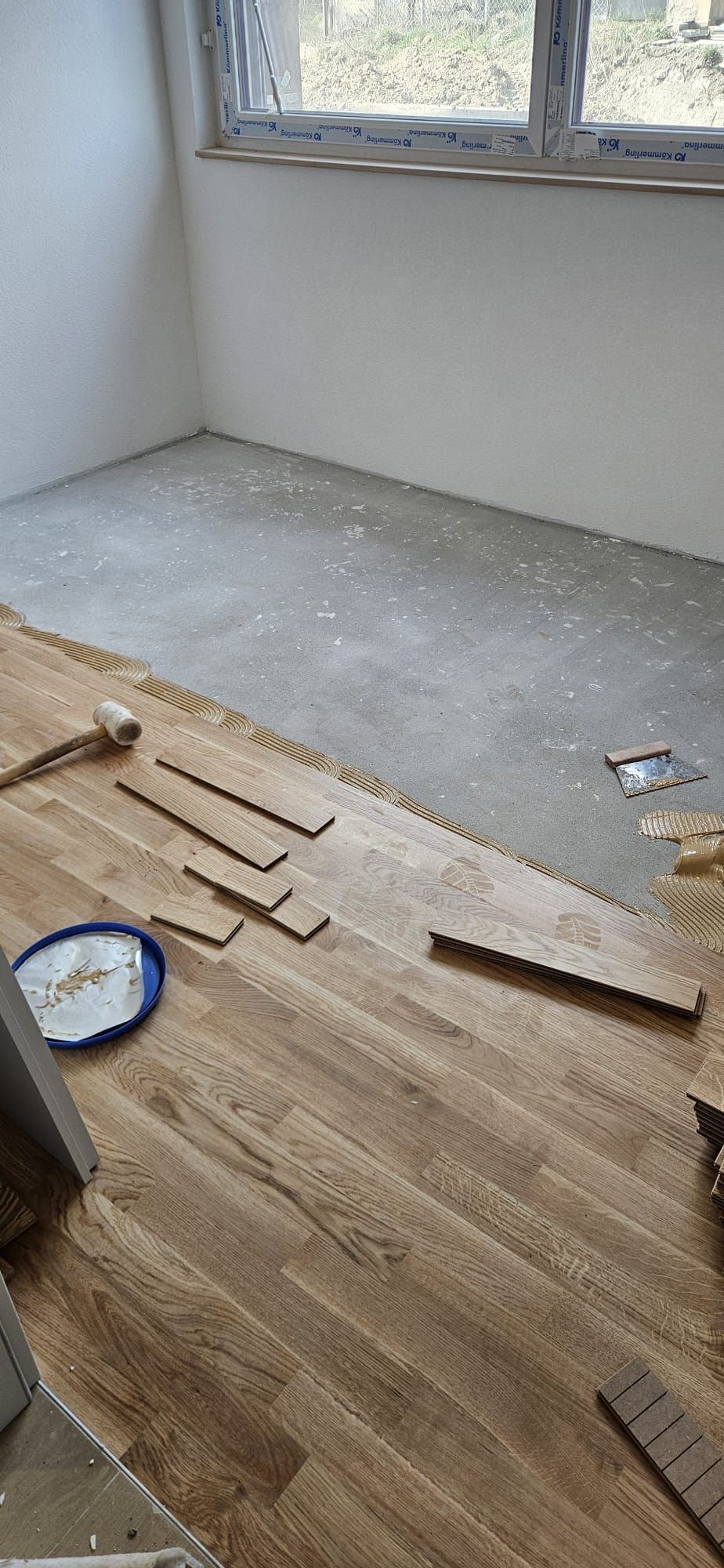 Pose d'un parquet en bois clair dans une pièce avec une dalle de béton et des outils éparpillés.