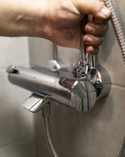 Käsi kiristää laatoitetun seinän kromiseen kiinnitetyn suihkuhanan jakoavaimella.