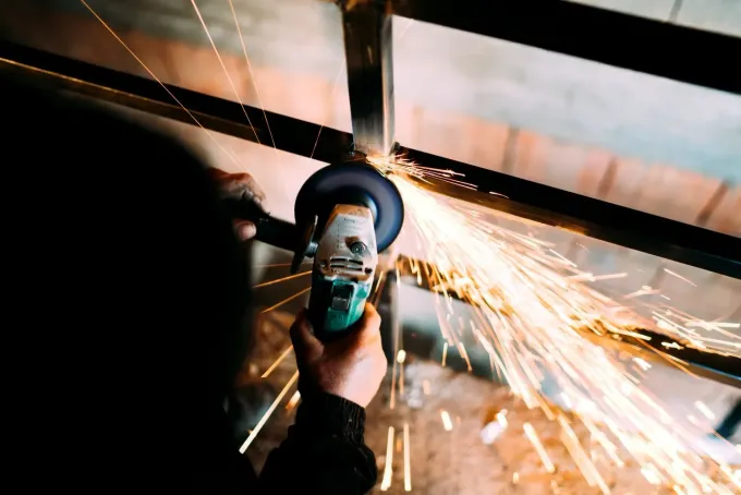 Persona que utiliza una amoladora, saltan chispas mientras trabaja en un marco de metal en un entorno poco iluminado.