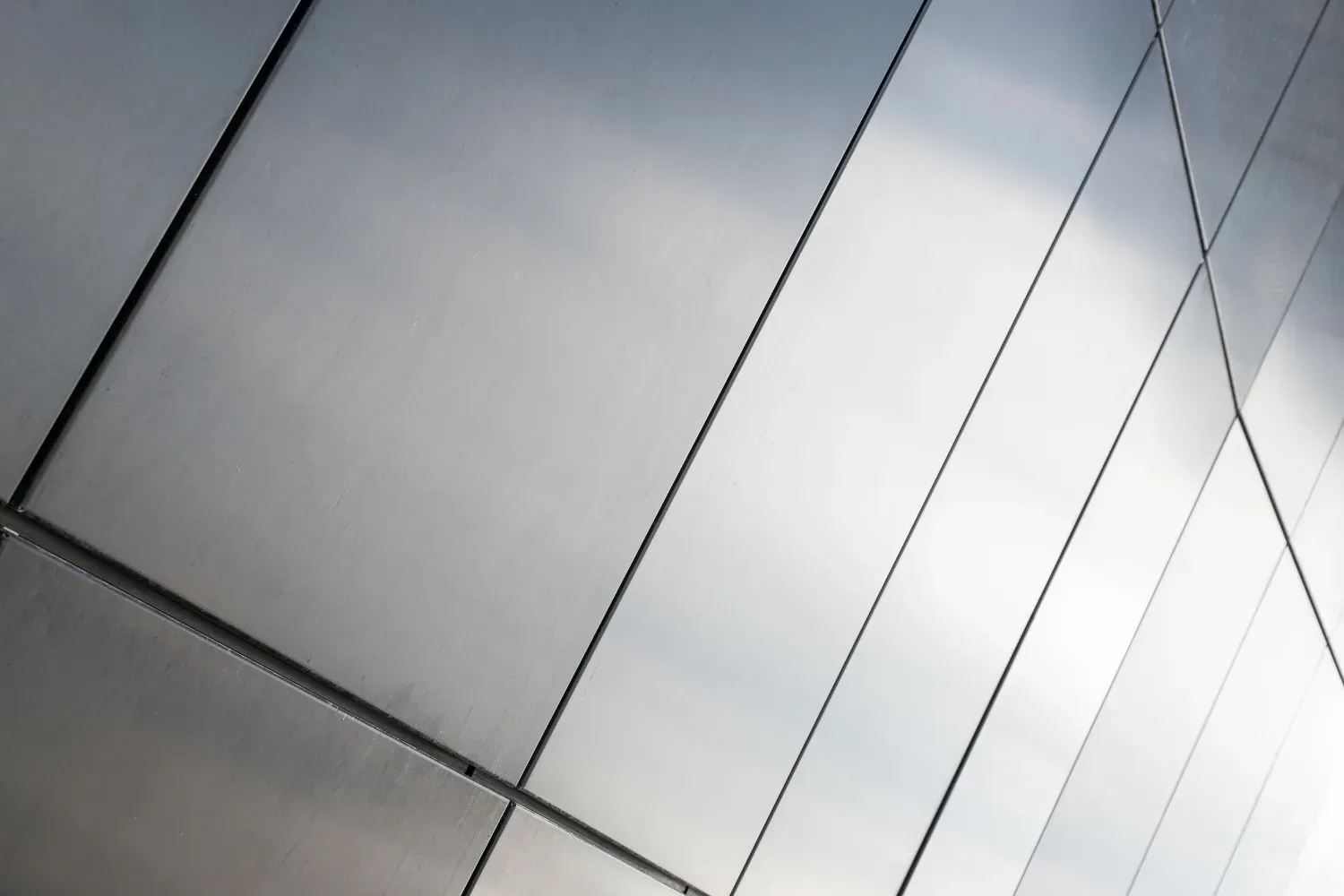 Paneles metálicos brillantes en la fachada curva de un edificio. Las líneas diagonales crean un patrón geométrico.