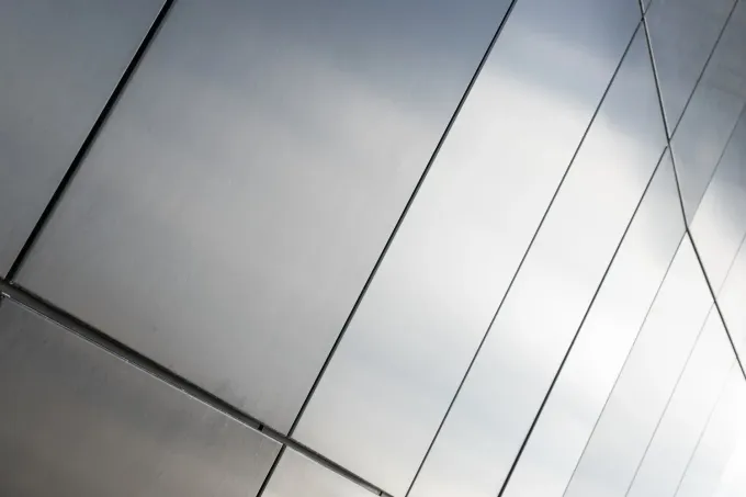 Paneles metálicos brillantes en la fachada curva de un edificio. Las líneas diagonales crean un patrón geométrico.