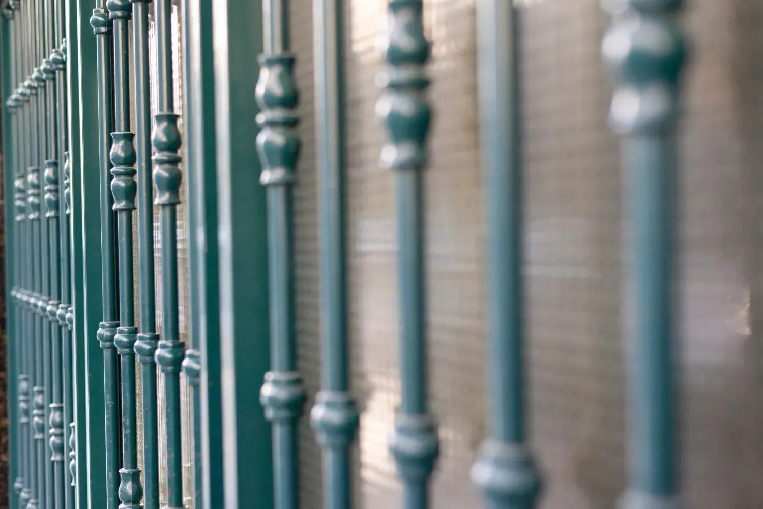 Valla metálica verde con barrotes verticales decorativos.