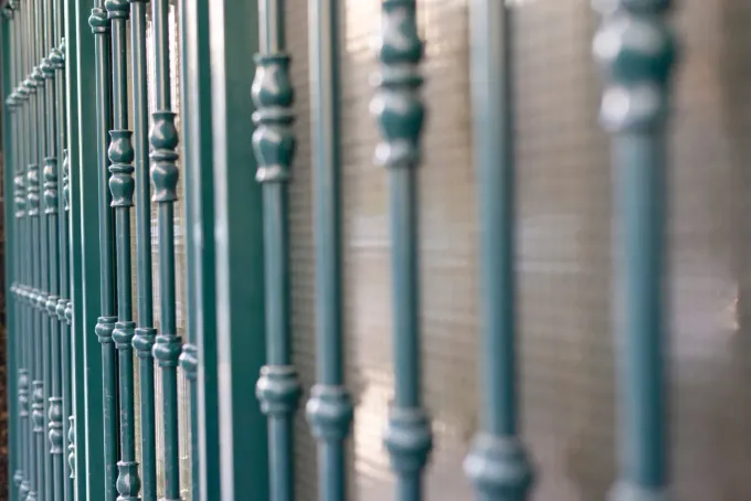 Valla metálica verde con barrotes verticales decorativos.