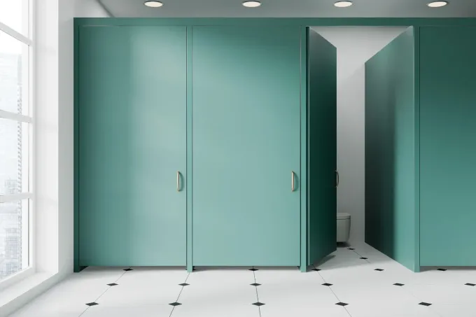 Cabinas de baño color verde azulado con una puerta abierta, piso de baldosas blancas y negras, ventana.