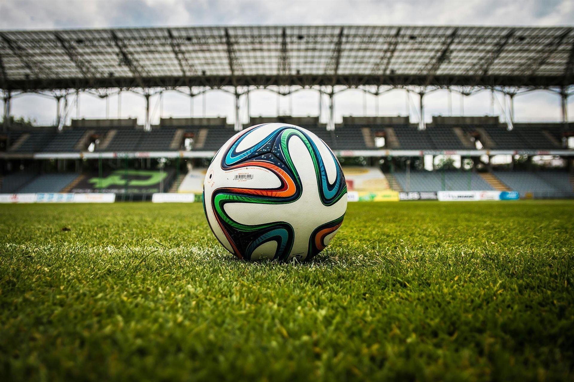 A soccer ball is sitting on the grass in front of a stadium.