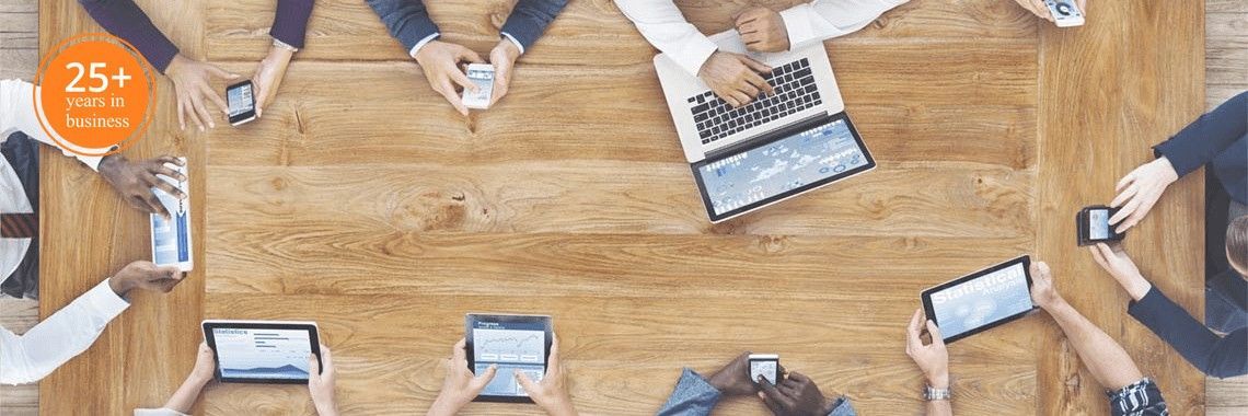 Des personnes assises autour d'une table en bois, certaines utilisant des téléphones, des tablettes