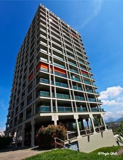 Immeuble d'appartements de grande hauteur avec façade en béton armé et balcons sous un ciel bleu.