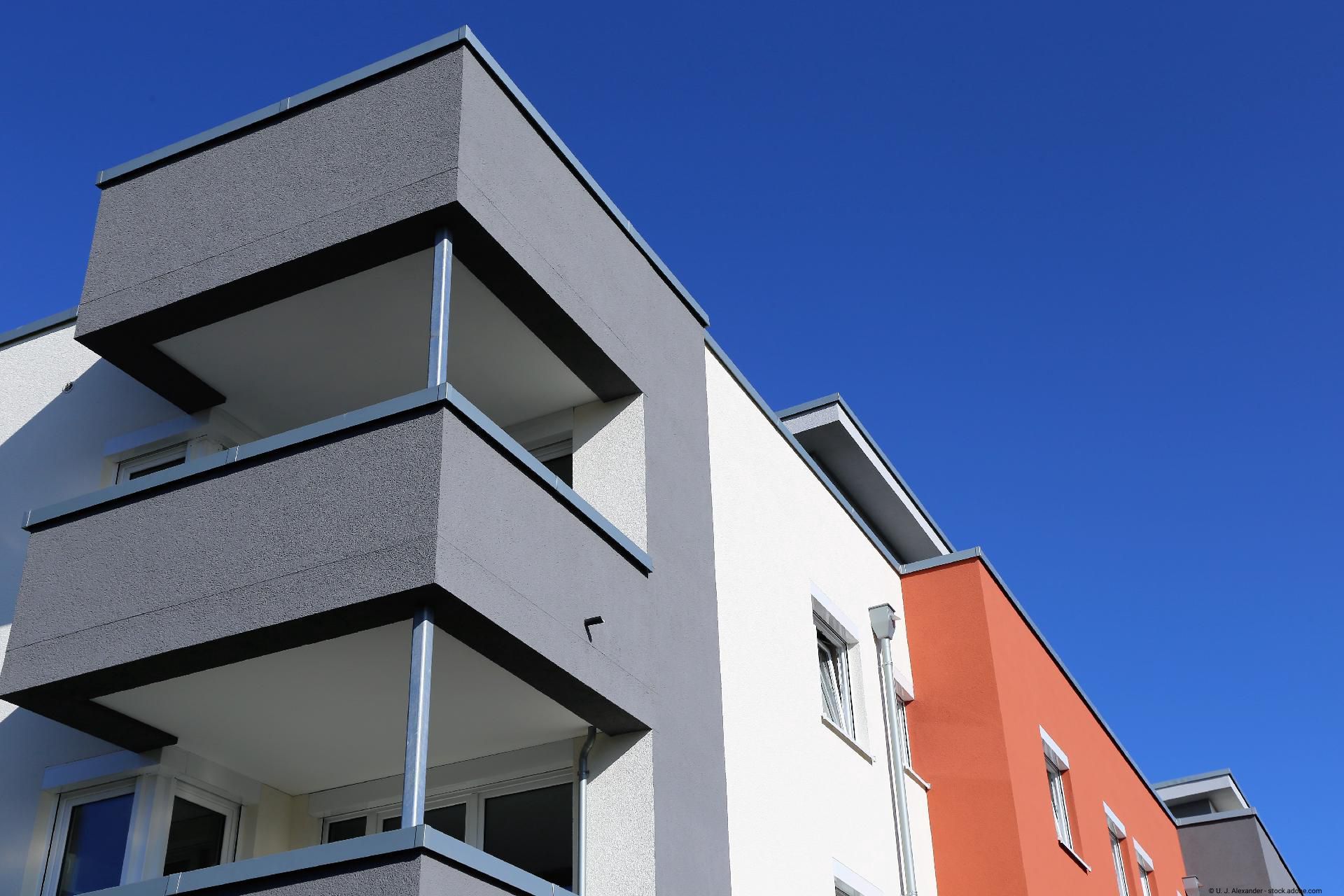 Moderne Hausfassade mit grauen Balkonen vor blauem Himmel.