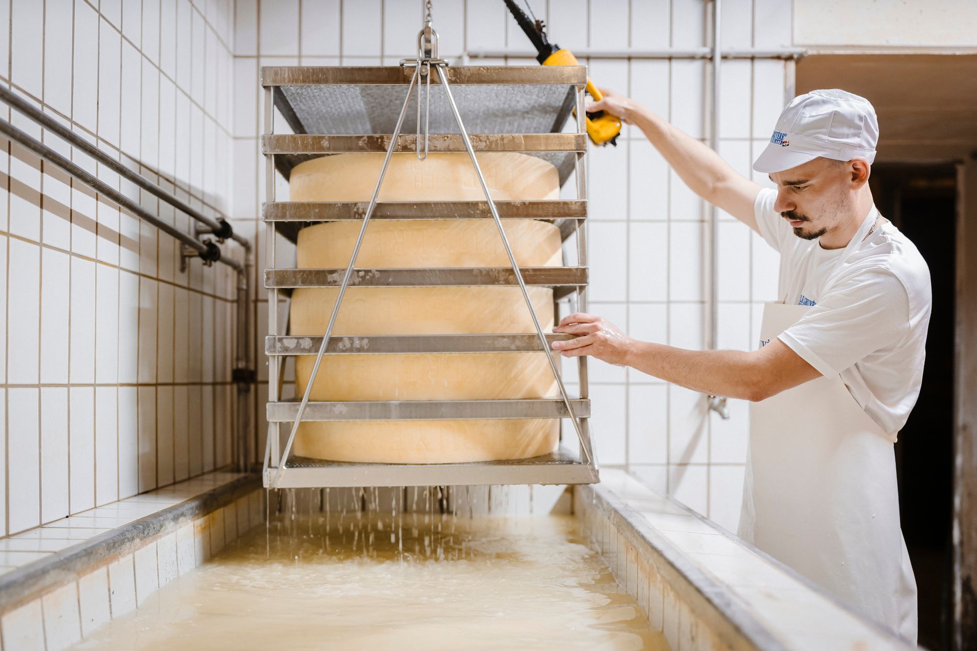 Cuisine industrielle avec cuves en acier inoxydable, tuyaux et sol en béton humide, avec un ouvrier en tenue blanche.