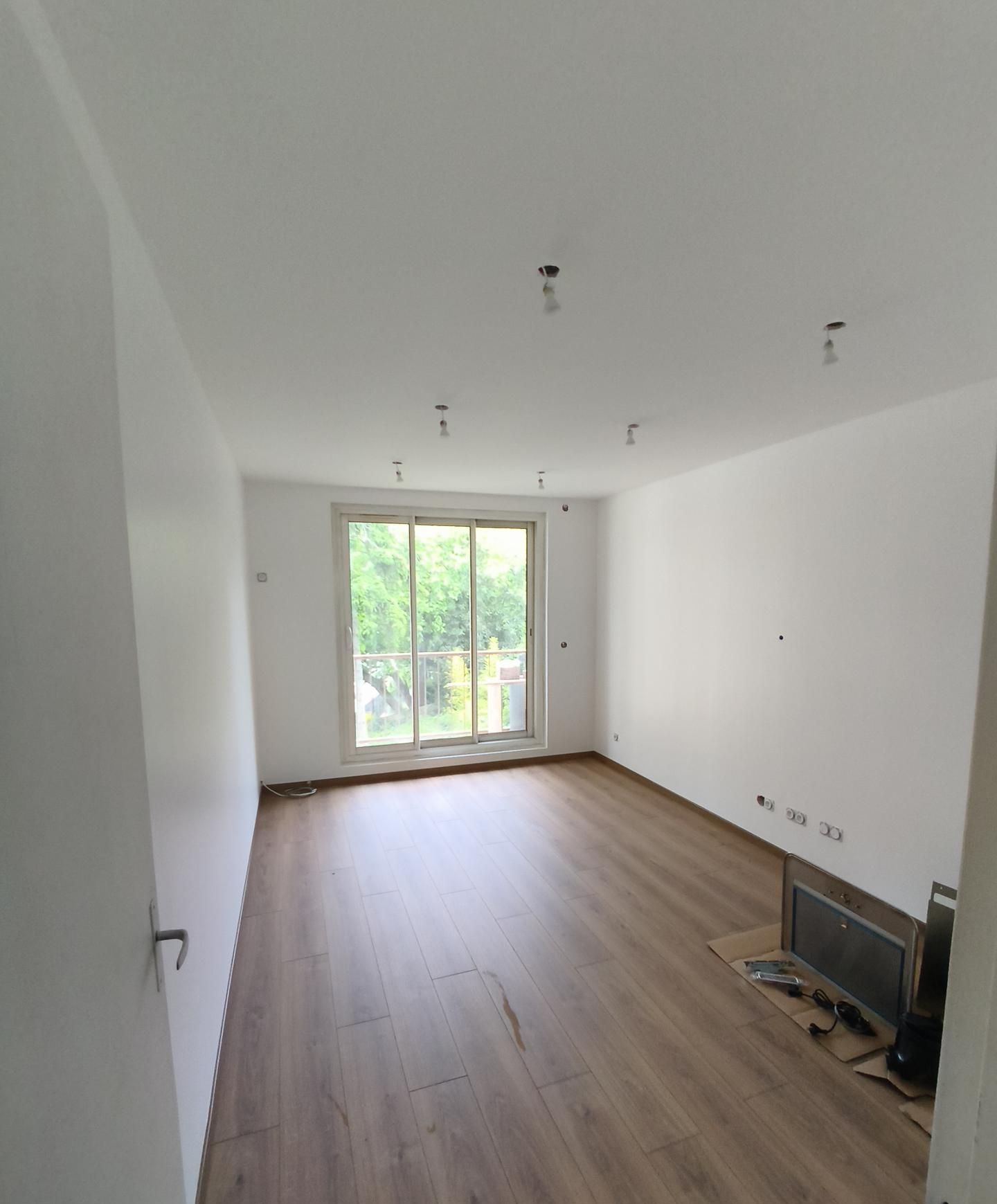 Pièce vide avec parquet clair, murs et plafond blancs.