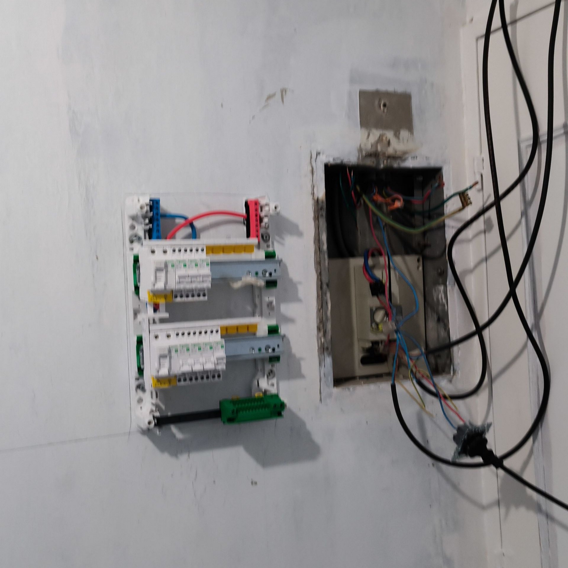 Des composants électriques fixés au mur, notamment un panneau avec des fils et des disjoncteurs, et une boîte électrique ouverte.