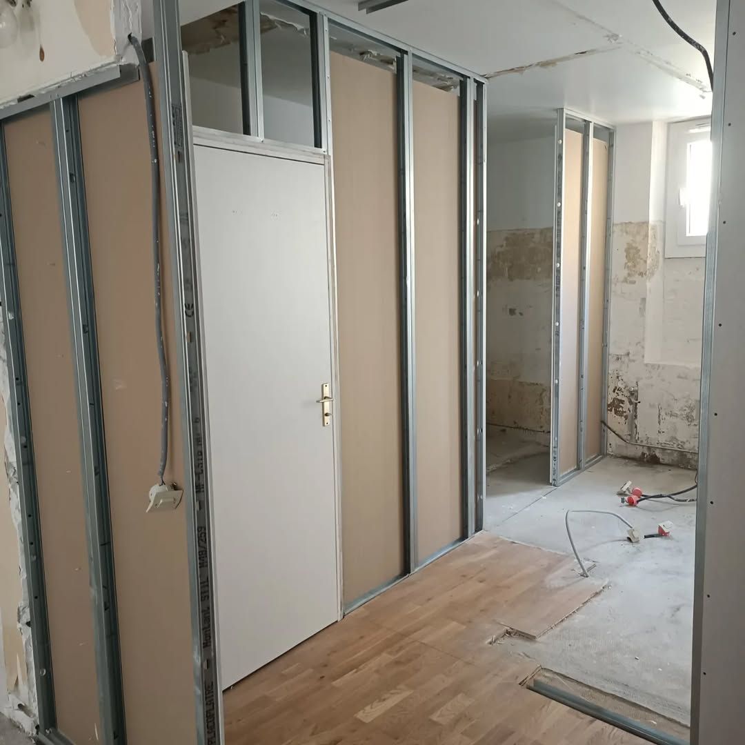 Intérieur en cours d'aménagement avec cloisons sèches, porte et câblage apparent.